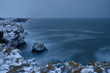 Powerful sea waves breaking on the rocky coast. Long exposure winter seascape at sunset. 