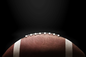 American football ball on black background illuminated by the light