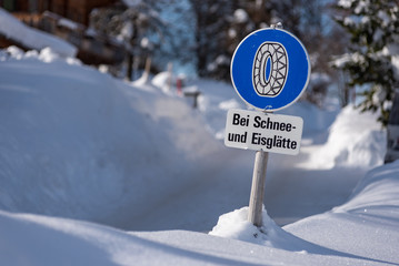 Chain traffic sign: Bei Schnee und Eisglätte. Blue warning information:  Snow chain obligation, Winter time and winter services. Snow covered road, trees. Styria, Austria - 302538662