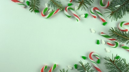 Christmas season day table still frame, close up with various candy canes and holiday sweets arranged on white background. New year decoration with various sprinkles and fir, pine branches.