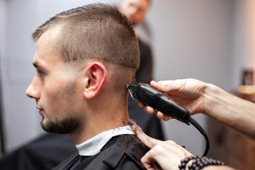 young guy makes a short haircut in a barbershop with a trimmer, close-up