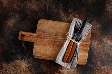 Cutlery on the plate on dark brown background. Fork and table-knife with wooden handles on linen...