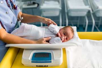 Young nurse working in maternity ward. She measuring weight and wrapping the newborn baby.