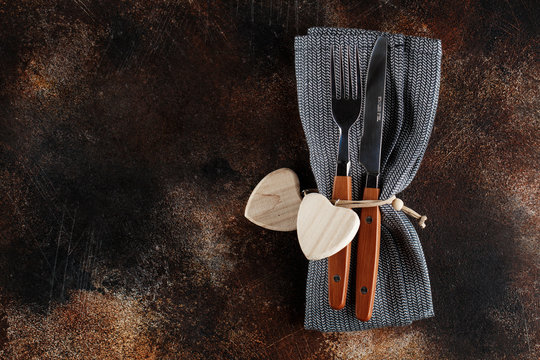 Cutlery on the plate on dark brown background. Fork and table-knife with wooden handles on linen napkin and wooden board