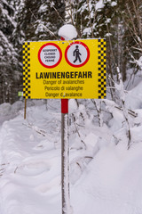 Yellow-black warning sign and signs in German, English, Italian and French: Closed, Danger of avalanche. A forest, snow-covered road in the mountains. Styria, Austria, Europe