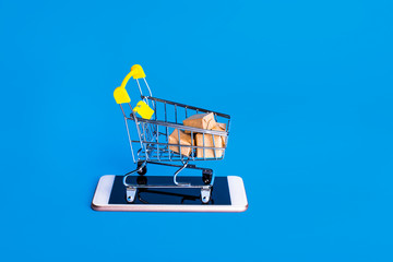 Online marketplace delivery. Boxes in a shopping cart on smartphone against blue background. Demonstrate fast order delivery. Shop sales, black friday concept
