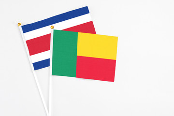 Benin and Costa Rica stick flags on white background. High quality fabric, miniature national flag. Peaceful global concept.White floor for copy space.