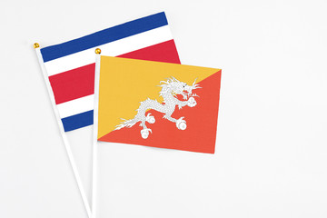 Bhutan and Costa Rica stick flags on white background. High quality fabric, miniature national flag. Peaceful global concept.White floor for copy space.