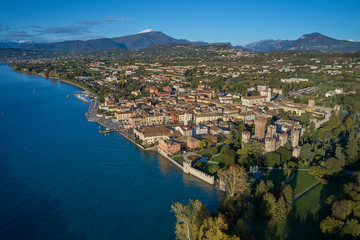 Naklejka na ściany i meble Aerial view of Lake Garda and the city center of Lazise, Italy. Autumn season, blue sky, Alps on the horizon, snow in the mountains