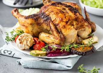 Baked whole chicken with vegetables, thyme and salad on a white ceramic plate. 