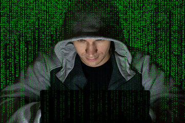 The villain, a computer hacker in the hood at the computer on a background of binary code