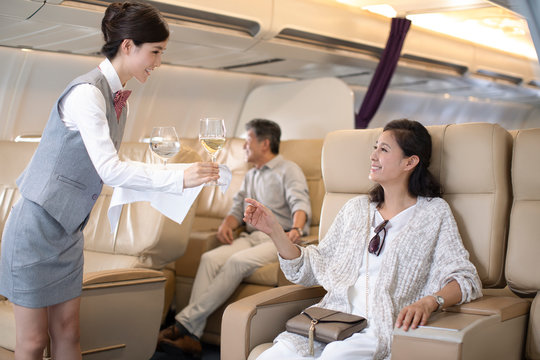 Chinese flight attendant serving wine to mature woman
