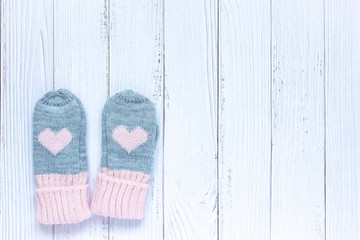 Children's winter accessories, warm knitted mittens - gray with pink hearts on white wooden background. Flat lay, copy space for text.