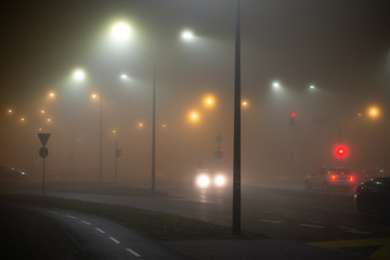 Cars driving in the tick fog on the city streets at night