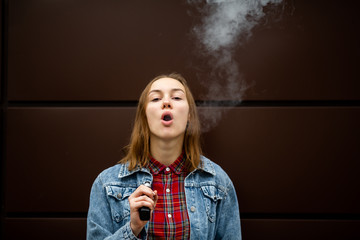 Vaping teenager. Young pretty white girl in casual clothes smoking an electronic cigarette opposite...