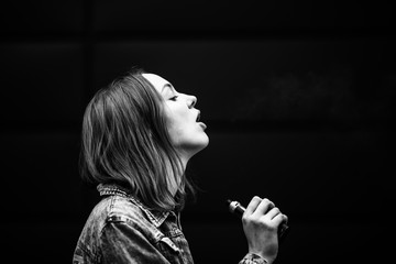 Vaping teenager. Young pretty white girl in casual clothes smoking an electronic cigarette opposite...