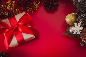 New Year's gift with a red ribbon in craft brown paper. Christmas composition of cones, tinsel and gifts on a red background.