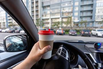 Closeup of a young man car driver drinking coffee, hand holding a paper white coffee Cup with a red...