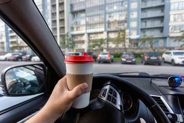Closeup of a young man car driver drinking coffee, hand holding a paper white coffee Cup with a red...