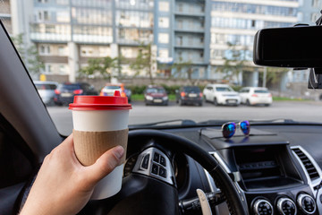 Closeup of a young man car driver drinking coffee, hand holding a paper white coffee Cup with a red...