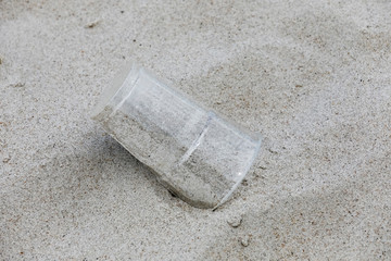 Fototapeta na wymiar Used plastic mug thrown away on a sandy beach