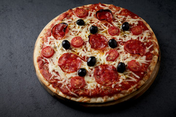 Pizza with chorizo, mozzarella cheese, cherry tomatoes, black olives and oregano. Home made food. Concept for a tasty and hearty meal. Black stone background. Close up.