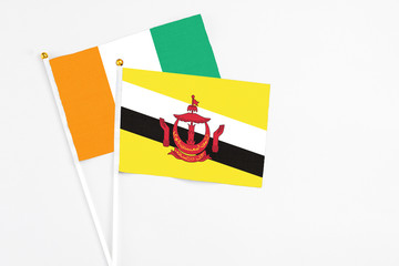 Brunei and Cote D'Ivoire stick flags on white background. High quality fabric, miniature national flag. Peaceful global concept.White floor for copy space.