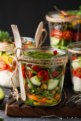 Poke salad with vegetables in a jar with fork on wooden rustic b