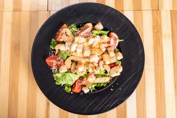 Caesar salad on a black plate, on a wooden background.