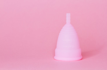 Close up of a young woman hands holding reusable pink silicone menstrual cup on pink background