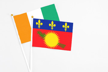 Guadeloupe and Cote D'Ivoire stick flags on white background. High quality fabric, miniature national flag. Peaceful global concept.White floor for copy space.