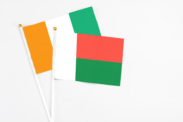 Madagascar and Cote D'Ivoire stick flags on white background. High quality fabric, miniature national flag. Peaceful global concept.White floor for copy space.
