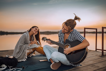 Attractive guy playing a guitar to his girlfriend by the river