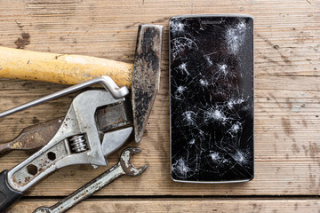 Smartphone repair concept. Crashed smartphone screen with grunge repairing tools on wooden...