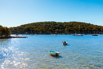 Small boats anchored in shallow calm crystal clear blue and green water on a sunny summer day, looking into the sun. Landscape image with copy space. Church Point, Pittwater, Sydney, Australia.