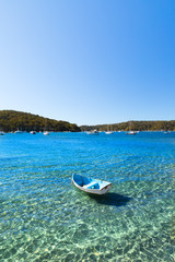 A small blue and white wooden row boat anchored in shallow calm water on a sunny summer day. Vertical portrait image with copy space.