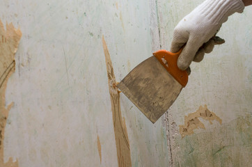Preparing the wall for painting or sticking new wallpaper. Man in gloves with a scraper in the process of removing old wallpaper. wetted with a special solution surface