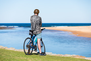 An unidentifiable man on a blue bicycle sits by the sea at the beach on a sunny day. Copy space.