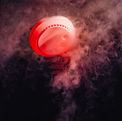 A household home fire detector alarm on the ceiling in a darkened room at night detects rising smoke to protect people asleep in their home.