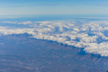 clusters of white clouds visible from above in the sky and mountains