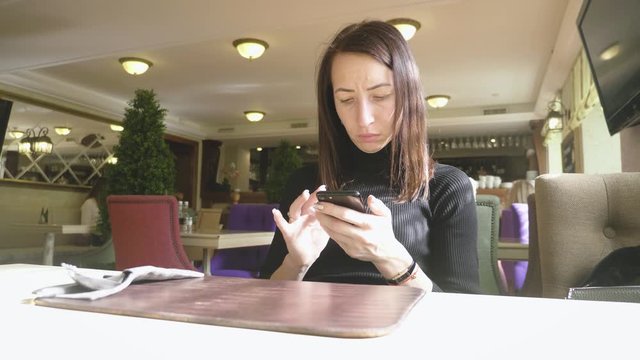 Young wonam use mobile phone while sitting in comfortable coffee shop during work break, charming happy female reading fashion news on cell telephone during breakfast in restaurant.