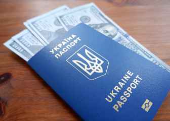 Ukrainian biometric passport and dollars. Ukrainian passport on a wooden background, top view. Document for traveling abroad in blue light