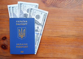 Ukrainian biometric passport and dollars. Ukrainian passport on a wooden background, top view. Document for traveling abroad in blue light