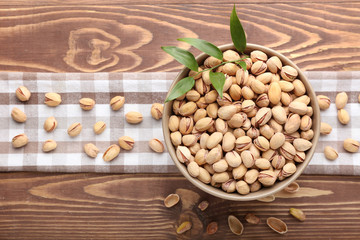 Bowl with tasty pistachio nuts on wooden background