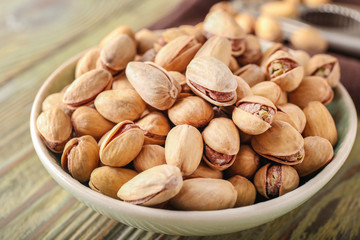 Bowl with tasty pistachio nuts on table, closeup