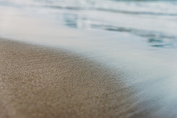 Small waves reach the shore of a serene beach and wet the fine sand, background of tranquility and vacations, at sunset.