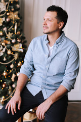 Charming smiling man next to a Christmas tree. Portrait of a handsome happy young man