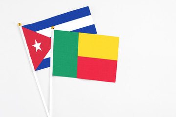 Benin and Cuba stick flags on white background. High quality fabric, miniature national flag. Peaceful global concept.White floor for copy space.