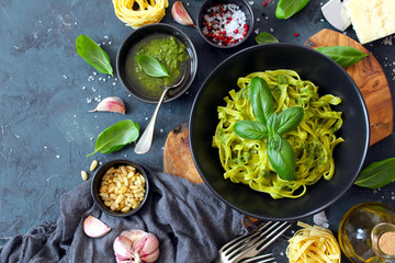 Pasta tagliatelle with pesto sauce and fresh basil leaves in black bowl. Top view with copy space.