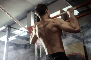Athlete muscular fitness male model pulling up on horizontal bar in a sport-club.